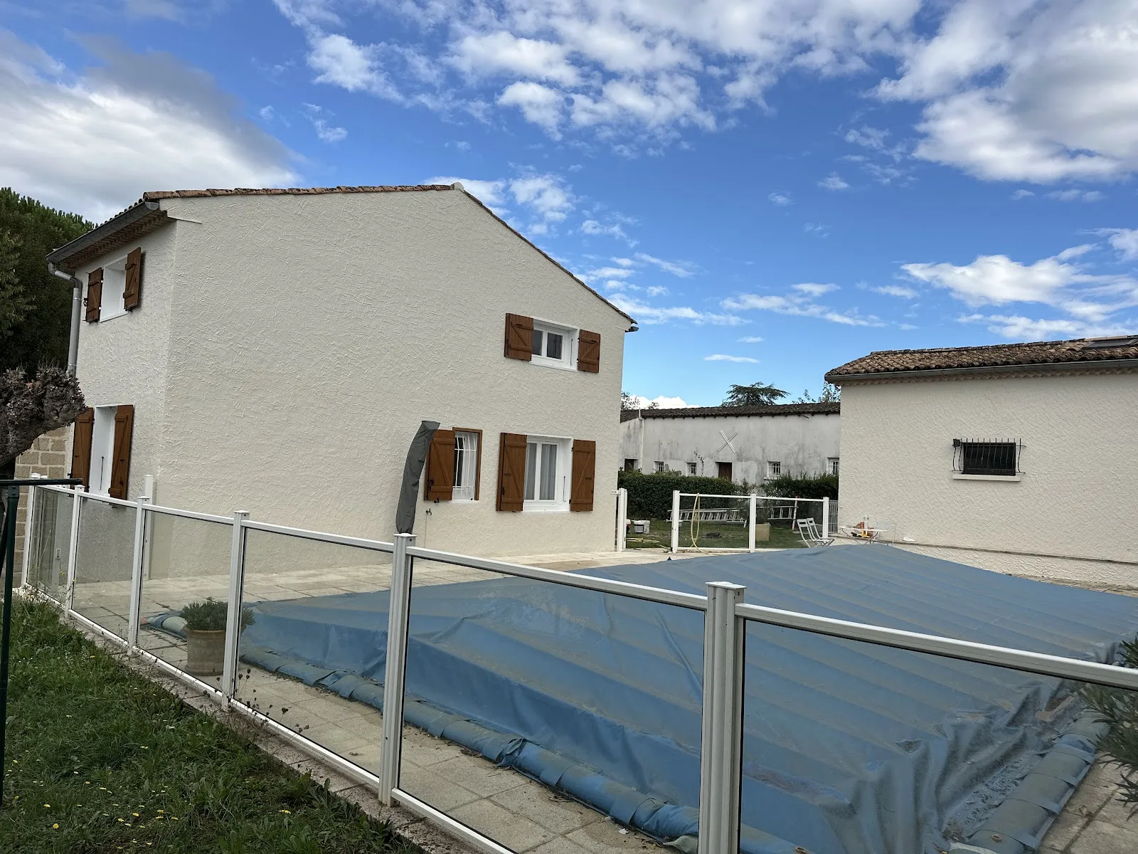 Maison rénovée aux murs clairs et volets bois, bord de piscine