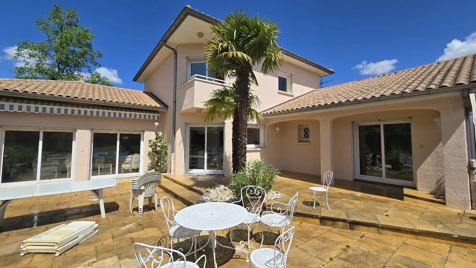 Terrasse et façade d'une villa aux teintes chaudes, palmier au centre