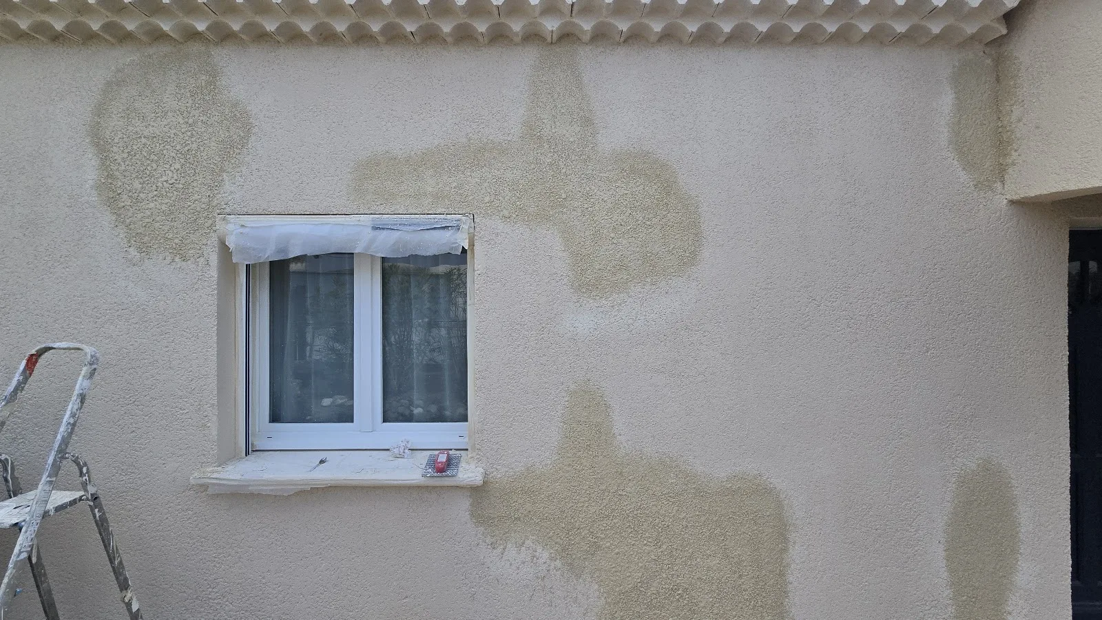 Reprise d'enduit de façade en cours autour d'une fenêtre protégée